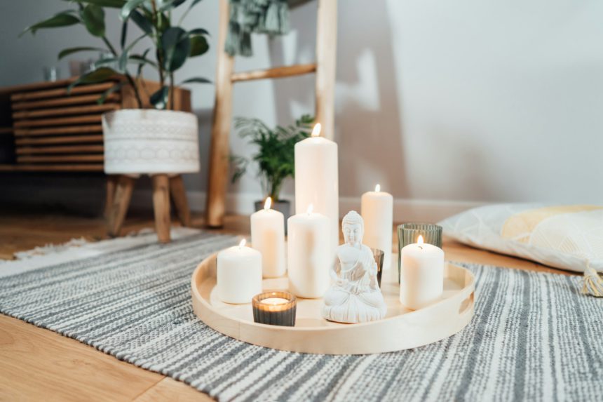 Wooden tray with burning candles and white Buddha statuette on the floor of modern interior.