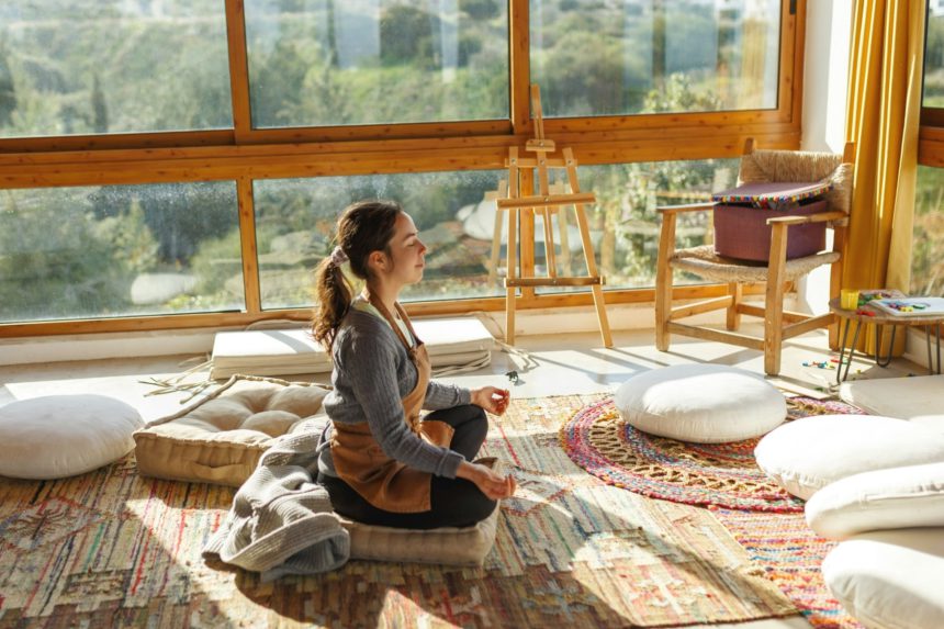 Young woman artist sitting on floor doing yoga exercise at art studio.Mindful activity